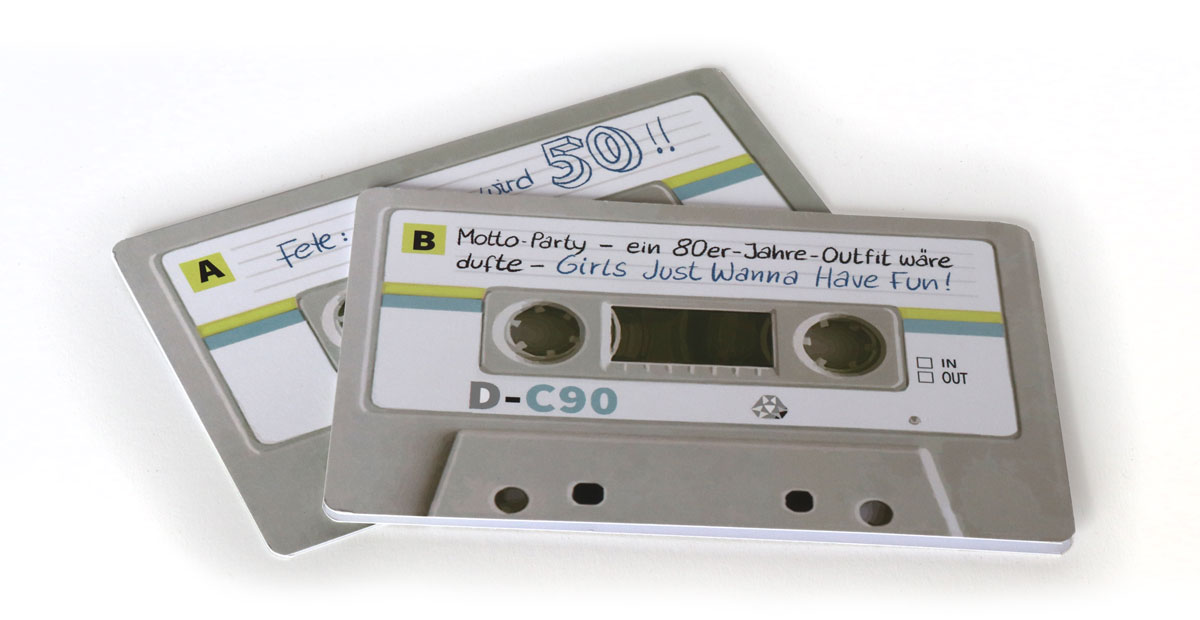 0021-Geburtstagseinladung80er-3 Zwei Klappkarten leicht versetzt übereinander, sodass man A- und B-Seite der „Kassette“ erkennt. Die Kassette ist technisch-hellgrau, mit weißen Schildern. Beschriftet mit Kugelschreiber.
